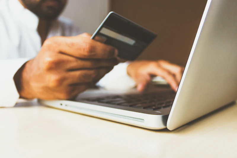 Hands holding a payment card at a laptop